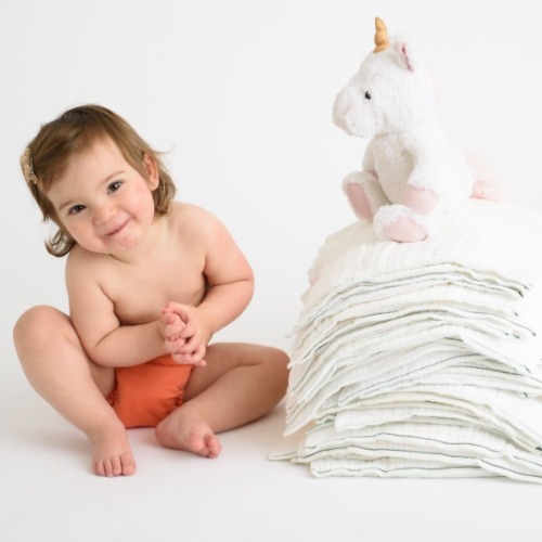 Young baby in cloth diaper sitting next to stack of cloth diapers and toy unicorn