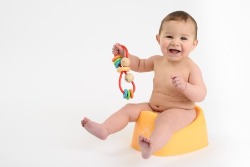 Infant sitting on plastic potty with toy in hand